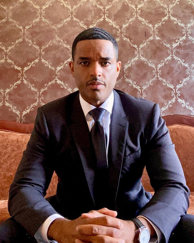 Larenz Tate in a white shirt and black coat.